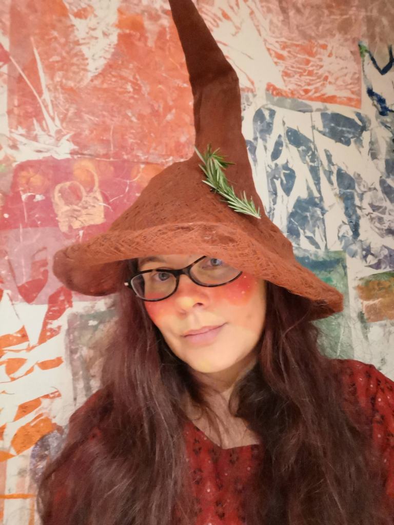 Spike looks at the camera with long brown hair over her brown blouse, wearing brown glasses and a brown hat with a very tall spike.
