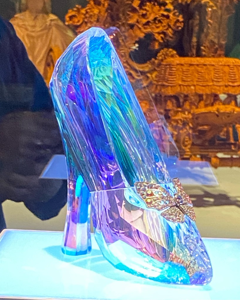 Glass slipper with gold butterfly on top, on shelf